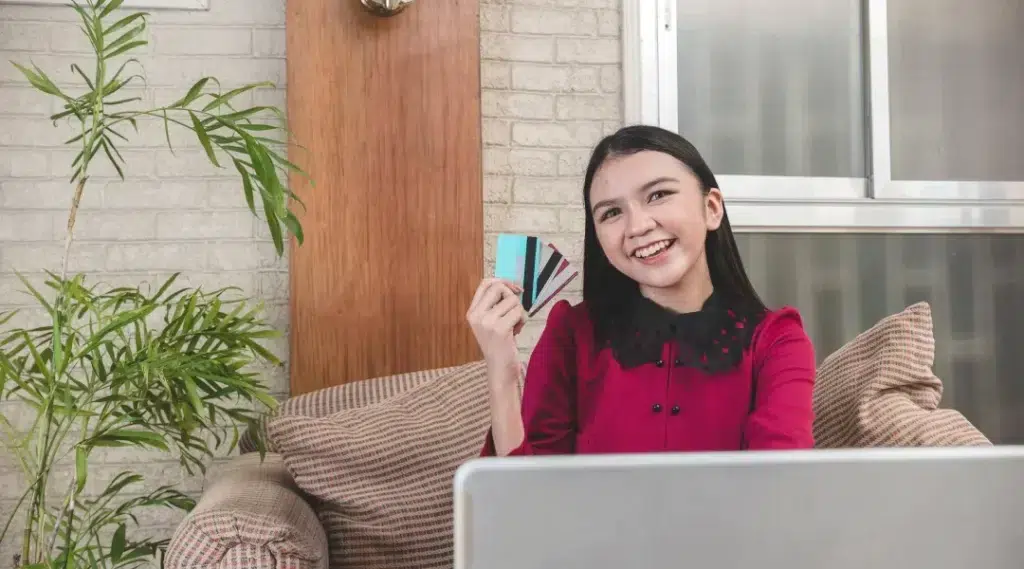 Une femme assise sur un canapé, utilisant un ordinateur portable avec une carte de crédit, affichant une bonne cote de crédit.