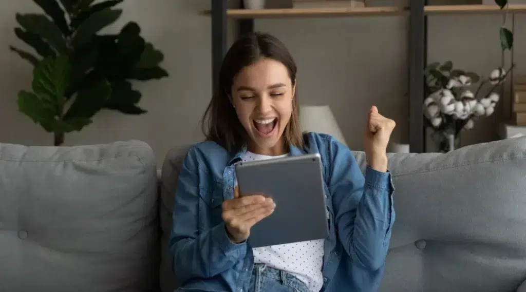 Une femme assise sur un canapé, tenant une tablette électronique, illustrant le prêt personnel à acceptation garantie.
